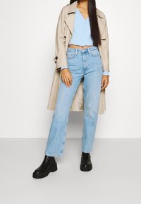 Beige trenssitakki, vaaleansininen lyhyt nappipaita, vaaleansiniset farkut ja mustat korolliset nilkkurit. Suorat farkut, joissa on lievä haalistuma.