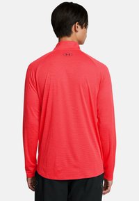 Langarmshirt in helder koraal, lichte stof met een gladde textuur. Heeft een halve rits kraag en subtiele horizontale strepen.