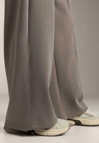 Sivé, voľné športové nohavice vyrobené z mäkkej tkaniny, s rovný strih, skombinované so svetlými, čalúnenými teniskami.