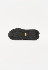 Semelle de chaussure en caoutchouc noir avec des profondes rainures pour l'adhérence, arborant un logo jaune et des motifs texturés pour une bonne prise et une durabilité.