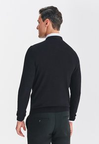 Czarny sweter wykonany na drutach z wysokim kołnierzem, długimi rękawami i ściągaczami. Tył ma gładką strukturę bez widocznych wzorów lub akcentów.