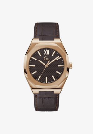 Hnedý kožený remienok s krokodílou textúrou, osmeruhlové puzdro v zlatej farbe, tmavý textúrovaný ciferník, zlaté hodinové značky a logo "Gc" v strede.