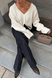 Cremfarbener V-Ausschnitt Oversized-Pullover, schwarze ausgestellte Jeans, braune spitze Mules und eine beigefarbene strukturierte Handtasche, alles auf Steinstufen arrangiert.