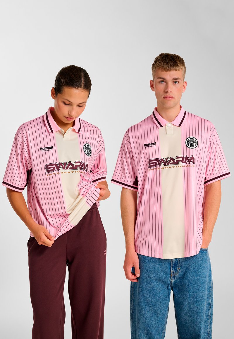 Lyserøde, stribede polo shirts med en cremefarvet midte og en sort krave, med logo og teksten "SWARM" i guld. Modellerne bærer afslappede bukser.