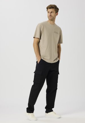 T-shirt en coton beige à manches courtes avec un petit logo imprimé. Associé à un pantalon cargo noir avec des poches latérales. Baskets blanches.