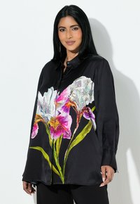 Sort satinbluse med blomsterdesign med livlige hvide og lyserøde irisblomster, grønne blade og knapper foran. Lange ærmer.