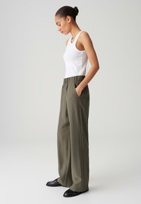 Pantalons larges vert olive avec une taille élastique et des poches latérales, associés à un débardeur blanc ajusté et des chaussures noires.