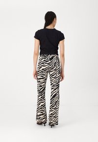 Black fitted t-shirt paired with high-waisted beige pants featuring a black zebra stripe pattern, flared leg design, and minimalistic detail.