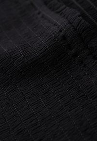 Close-up of black fabric with elastic waistband featuring vertical textured stripes and fine stitching details.