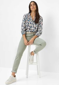 Hemd mit floralem Muster und Puffärmeln, hellgrüne, figurbetonte Hose und weiße Sneaker. Das Outfit zeichnet sich durch eine schlanke Passform und ein strukturiertes Design aus.
