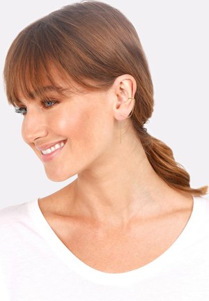 Ohrringe in Goldoptik mit einem gekrümmten Hoop-Design und einem geraden Tropfenelement. Das Model hat schulterlanges braunes Haar und trägt ein weißes Oberteil.