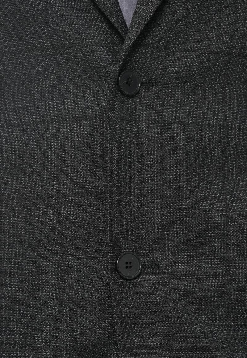 Dunkelgraue Anzugjacke mit feinem Karomuster, zwei schwarze Knöpfe, die geschlossen sind, und einem Blick auf den hellgrauen Hemdkragen.