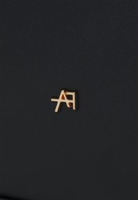Un matériau noir texturé présente un logo en métal doré "A" et un accent de design "A", positionné sur le côté.