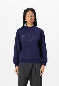 Sweatshirt azul-marinho com gola redonda e mangas balão, apresentando um design do horizonte de Paris e texto em letra cursiva "Paris, França" em uma impressão subtil.