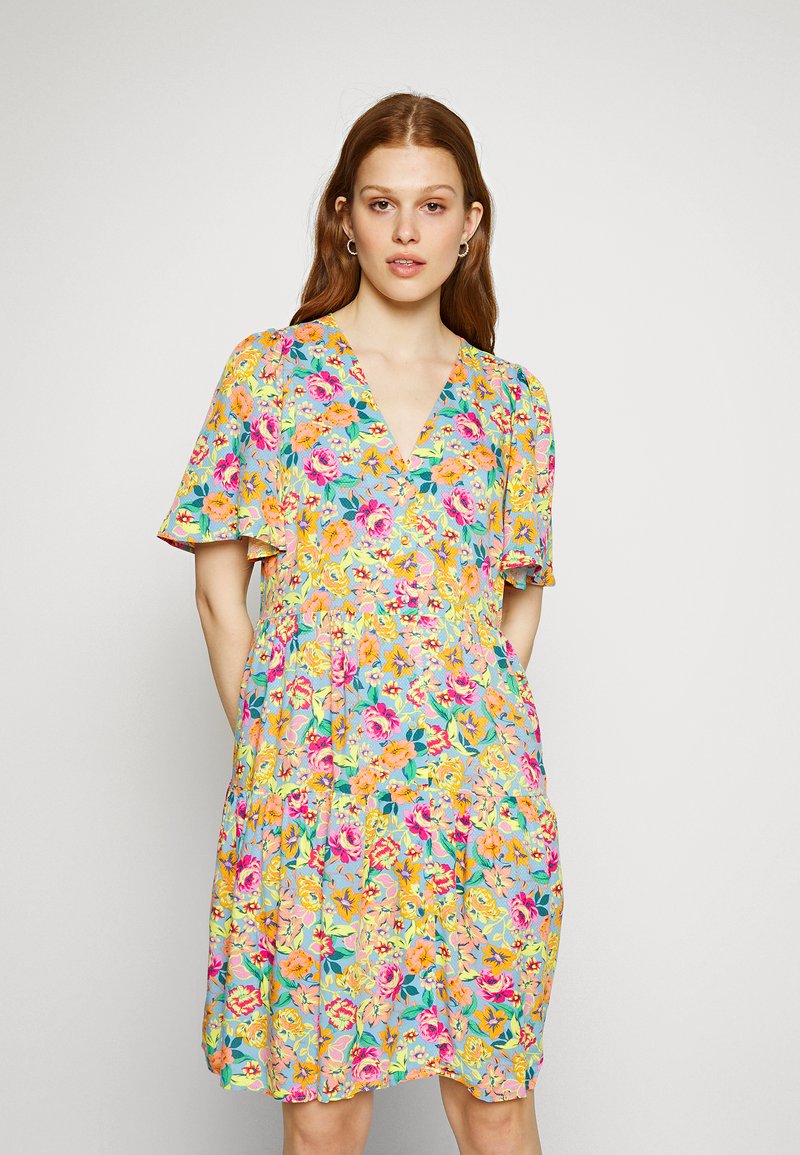 Vestido floral com decote em V, mangas leves e padrões de flores multicoloridas sobre um fundo azul claro; tecido leve.