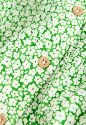 Groen stof met bloemenpatroon en kleine witte bloemen, voorzien van ronde houten knoppen. Zachte textuur, licht geplooide uitstraling.