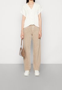 Vit kabelstickad cardigan med korta ärmar, beiga vida byxor, vita sneakers och en liten brun handväska med krokodilstruktur.