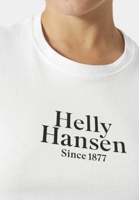 Camiseta de algodón blanca con cuello redondo, mangas cortas y texto impreso en negro "Helly Hansen Since 1877" en el frente.