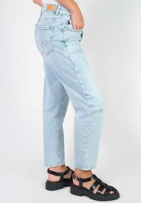 Lichtblauwe denim jeans met een relaxte pasvorm, voorzien van vijf zakken en een gestikt logo op de achterkant. Gecombineerd met zwarte sandaaltjes met banden.