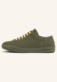 Baskets en daim vert olive avec des lacets jaunes, bout rond et semelle en caoutchouc vert moucheté. Présente un détail de couture et un logo sur le côté.