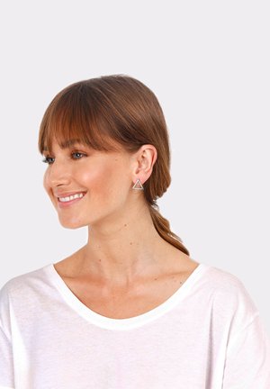 Pendientes de triángulo plateados con un diseño geométrico y un centro abierto, llevados por una persona con cabello castaño, vestida con una camisa blanca.