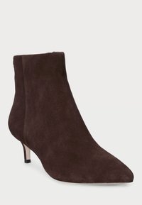 Botines de ante marrón con punta afilada, tacón bajo tipo kitten, y costuras decorativas. Accesorios metálicos en la parte trasera.