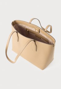 Geantă tote din piele bej cu mânere duale, un capac deschis și un buzunar interior cu fermoar căptușit cu țesătură matlasată; prezintă un design minimalist.