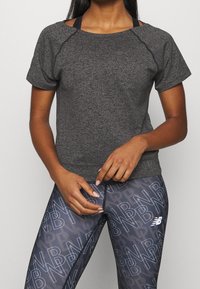 T-paita tummanharmaata urheilumallia, jossa on pyöreä kaula-aukko ja lyhyet hihat, valmistettu teksturoituneesta kankaasta, yhdistettynä kuviollisiin legginsseihin, joissa on logo.