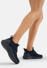 Marineblaue Sportschuhe mit einem strukturierten Mesh-Obermaterial, elastischen Kreuzgurten und einer Gummisohle mit einem Zickzack-Muster für besseren Halt.