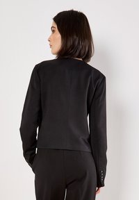 Czarna dopasowana marynarka z długimi rękawami, o eleganckim wzornictwie i wysokim kołnierzu. Posiada guziki na mankietach oraz gładką teksturę materiału.