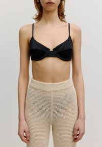 Zwarte satijnen bralette met een gestructureerd ontwerp en draaddetails, gecombineerd met beige gebreide broek met een losse, textuurweaving.