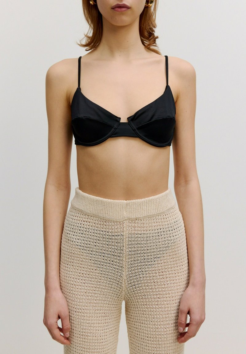 Zwarte satijnen bralette met een gestructureerd ontwerp en draaddetails, gecombineerd met beige gebreide broek met een losse, textuurweaving.