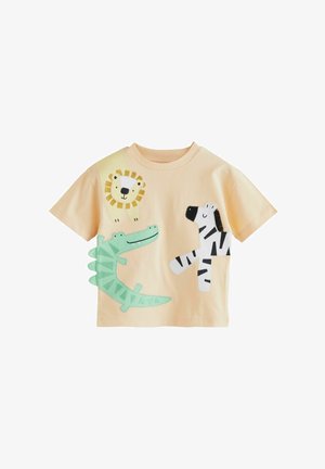 Īsām piedurknēm, gaiši oranžs kokvilnas t-krekls ar aplikācijām, kurās attēloti lauvas, zirga un krokodila dizaini melnā, baltā, dzeltenā un zaļā krāsā.