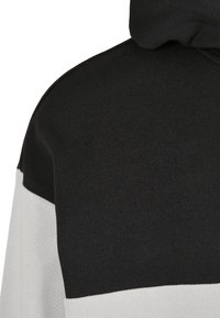 Svart och vit färgblockströja som visar axel- och övre ryggområde med synlig tygtextur och huva.