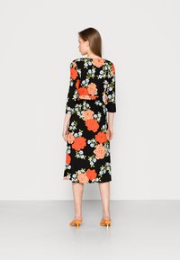 Vestido midi floral com fundo preto, grande padrão de flores laranja e azuis, mangas três quartos, cintura cinturada e mules de salto laranja.