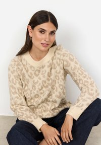 Beige tröja med en mjuk leopardtryckdesign, ribbad halsringning och manschetter, tillverkad av ett texturerat stickat material. Bärs med mörk denim.