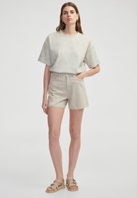 Světle šedé oversized tričko s malými tečkami, doplněné béžovými džíny s třásněmi a kapsami. Hnědé sandály.