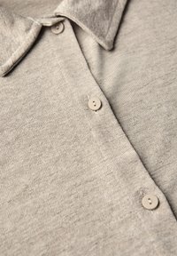 Beige stickad polo skjorta med en mjuk textur, en krage och tre runda knappar i matchande färg. Närbilden framhäver tyget.