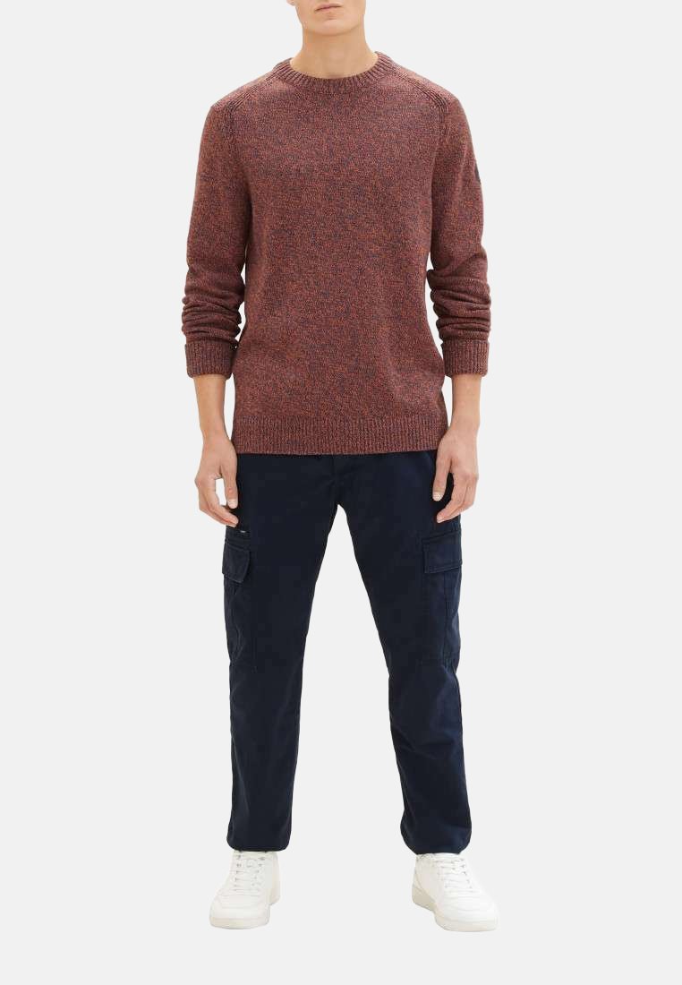 Pull en tricot à motifs rouge et bleu marine, avec un col ras de cou, des poignets et un ourlet côtelés, associé à un pantalon cargo bleu marine et des sneakers blanches.