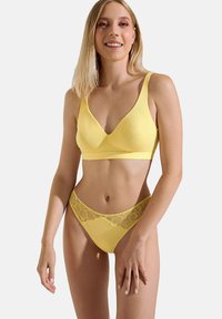 Ensemble de lingerie jaune composé d'un bralette triangulaire sans coutures et d'un string assorti. Le string présente des détails en dentelle le long de la taille.