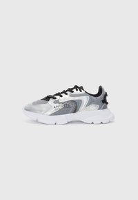 Des baskets Lacoste présentant un mélange de mailles argentées et de matériaux lisses. Des lacets noirs, une semelle épaisse blanche et des accents de logo complètent le design.