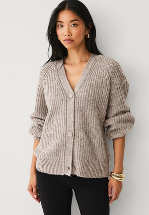 Beige knitted cardigan with a V-neck, button closure, and rolled sleeves. Textured fabric with a cozy, loose fit and two front pockets.