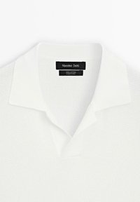 Polo shirt bianco in cotone con un tessuto textured e un classico colletto. L'etichetta riporta "Massimo Dutti."