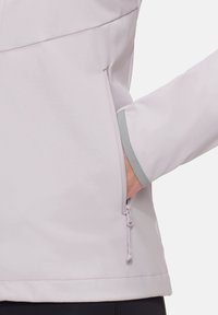 Ljuslila jacka med en ficka med dragkedja. Ärmen har en grå accent, och tyget ser slätt och något strukturerat ut.