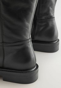 Schwarze Lederstiefeletten mit glatter Textur, ausgestattet mit horizontalen Nähten und einem niedrigen, gestapelten Absatz für ein robustes Design.