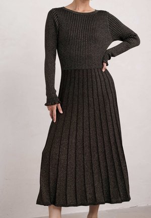 Femme portant une robe midi en maille côtelée à manches longues, corsage ajusté et jupe plissée en tissu métallique foncé sur fond uni.