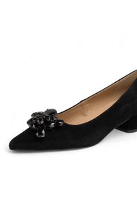 Décolleté in suede nero con punta affusolata e tacco basso. Presenta un'applique decorativa in cristalli neri sulla parte anteriore. Fodera interna liscia.