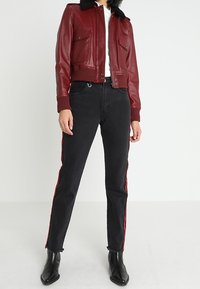 Körsbärsröd läderbombarjacka med en svart pälskrage, två framfickor, tillsammans med svarta jeans med röda sidostråk och svarta stövlar.