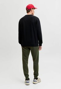 Sort sweatshirt med lange ærmer, grønne joggers med teksturdetaile på siden, rød kasket og beige sneakers med grå accenter.