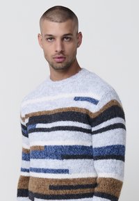 Gebreide trui met een ronde hals, meerkleurige strepen in bruin, blauw, zwart en wit, met een zachte, fluffige textuur.
